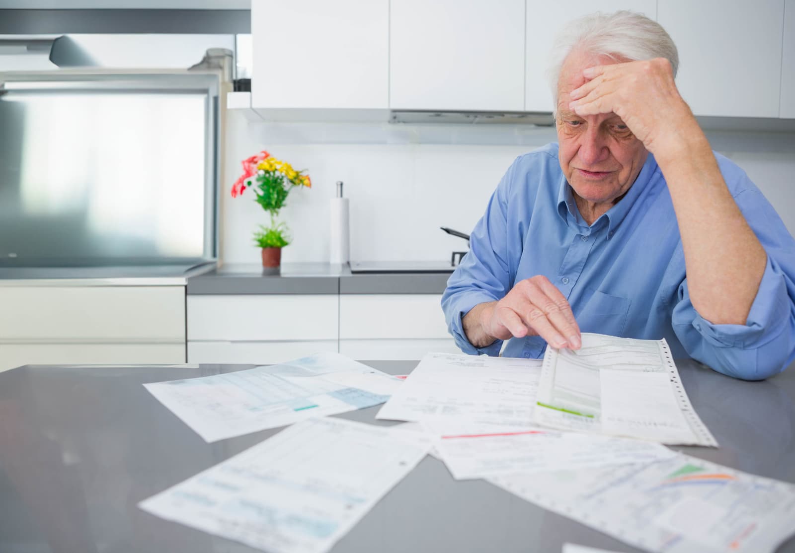 An older man going through bills and papers at his kitchen island