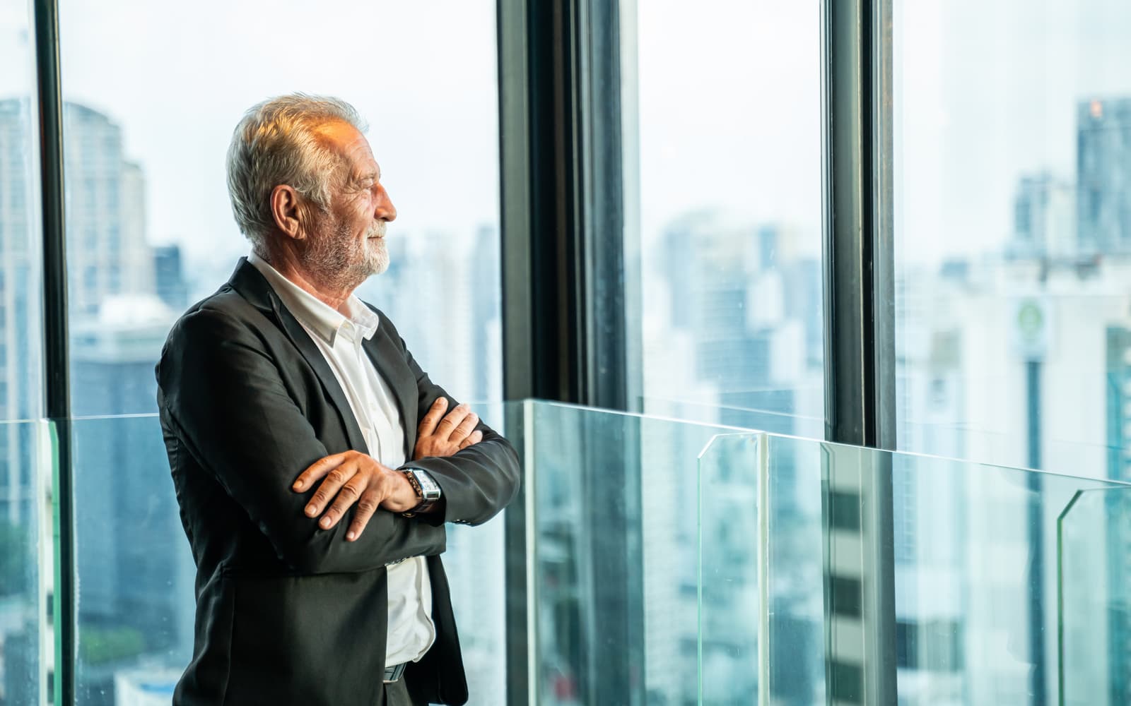 A grey-haired executive in a suit looking out of a window at the city