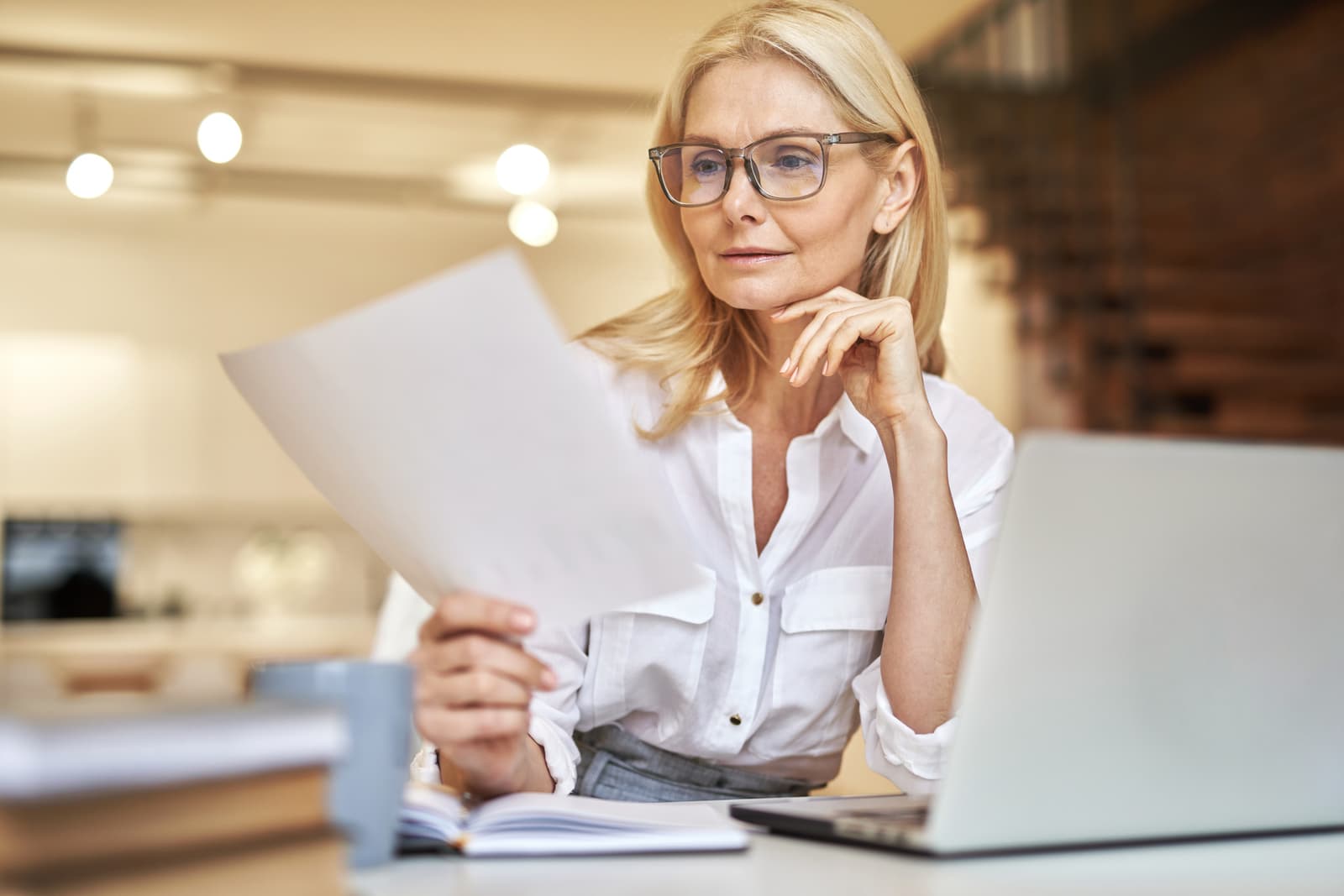 A mature businesswoman reading papers at her desk, weighing her options