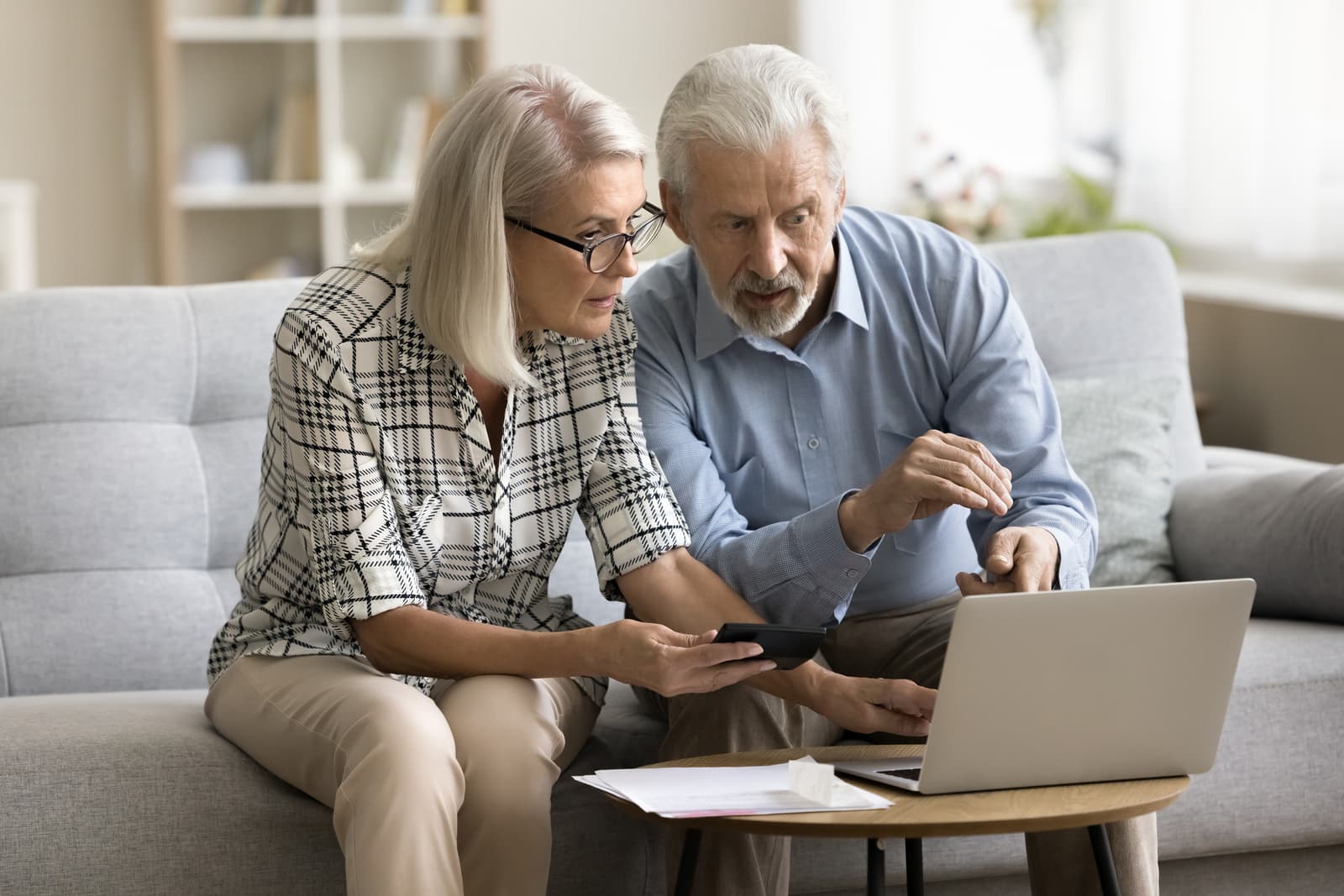 Serious senior married couple calculating domestic expenses, budget, fees, using online financial application on