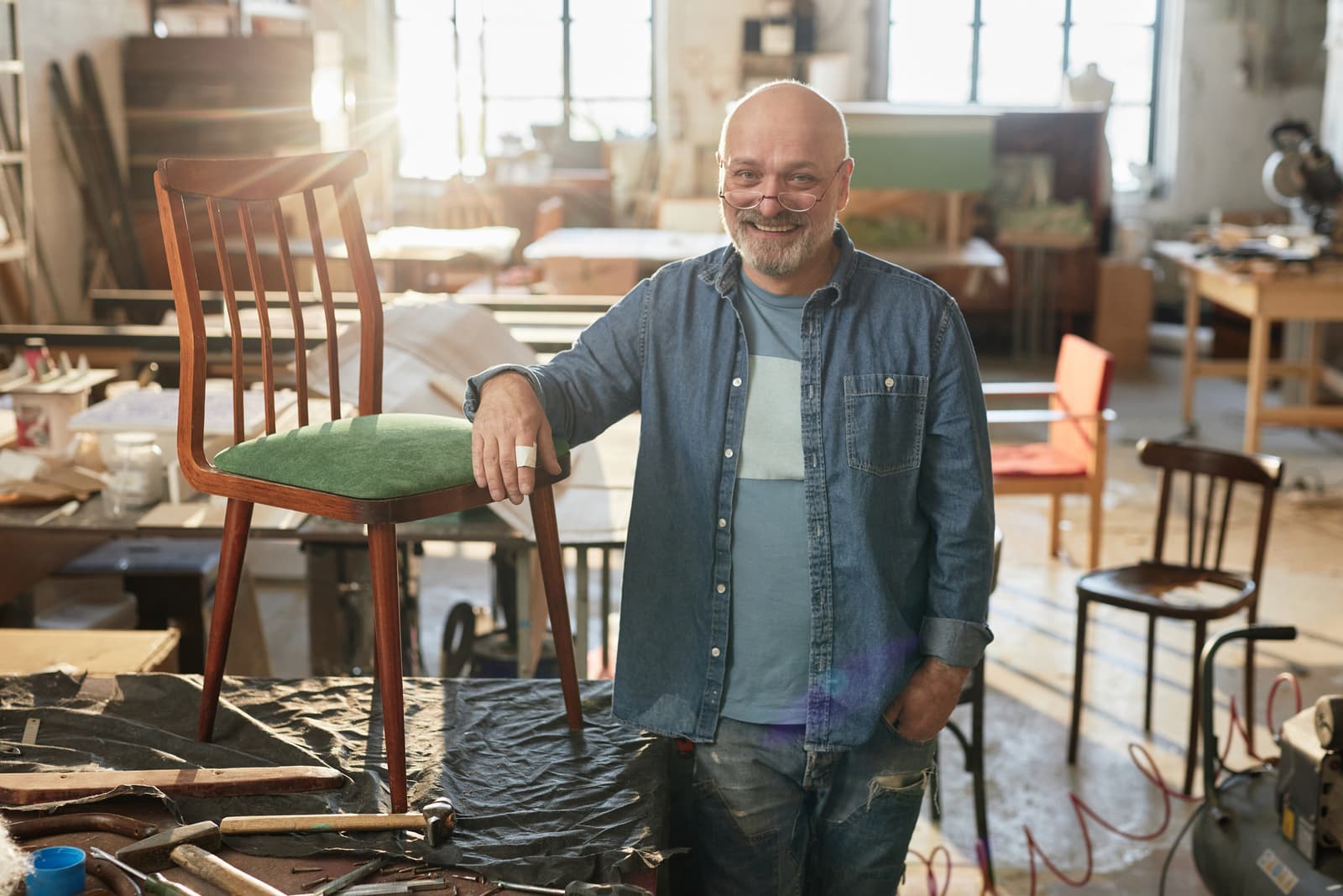 Waist up portrait of smiling senior carpenter looking at camera in furniture restoration workshop lit by sunlight, copy 