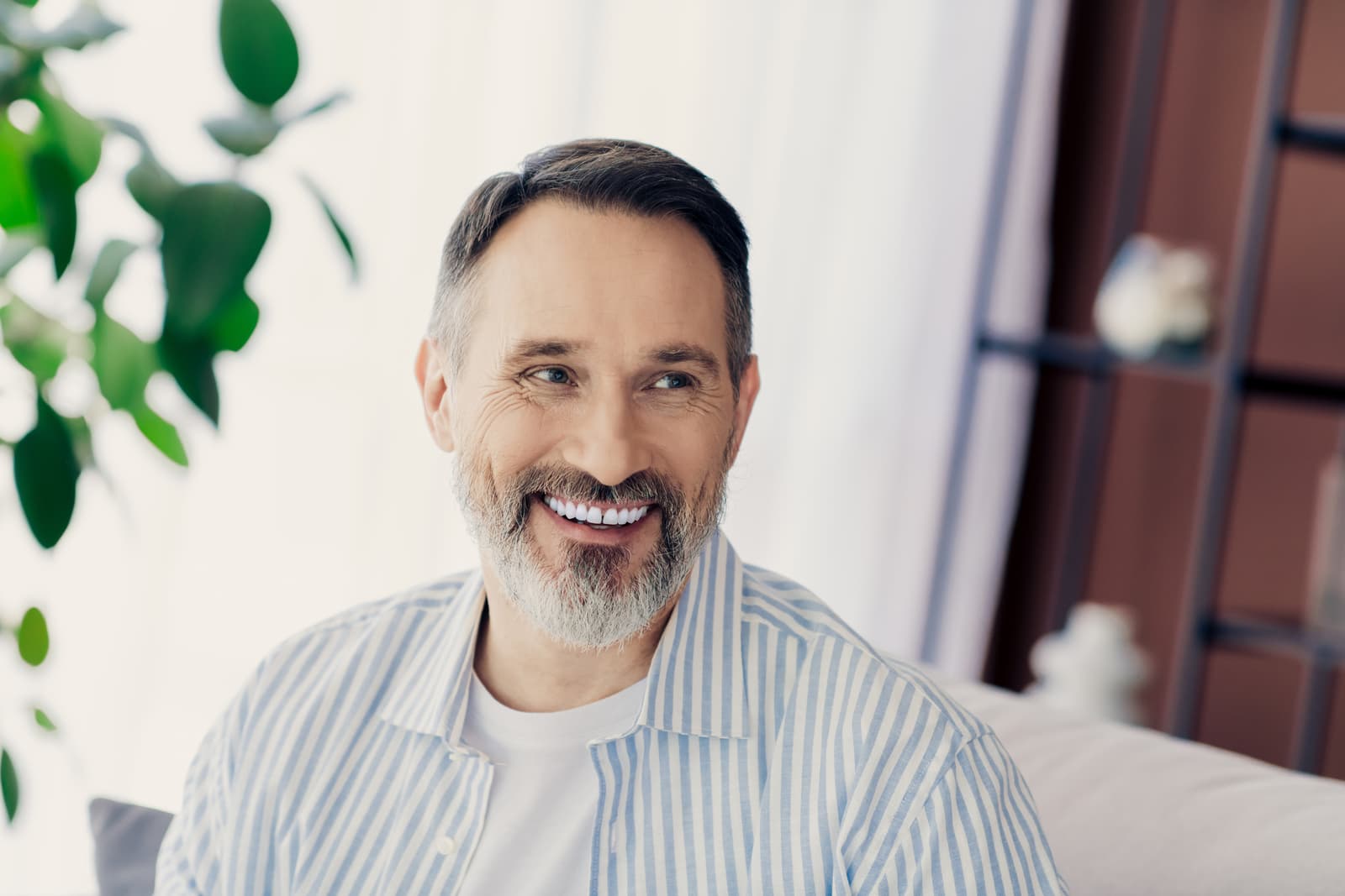 Confident mature man with a beard relaxing indoors wearing casual style shirt in a cozy setting with natural lighting