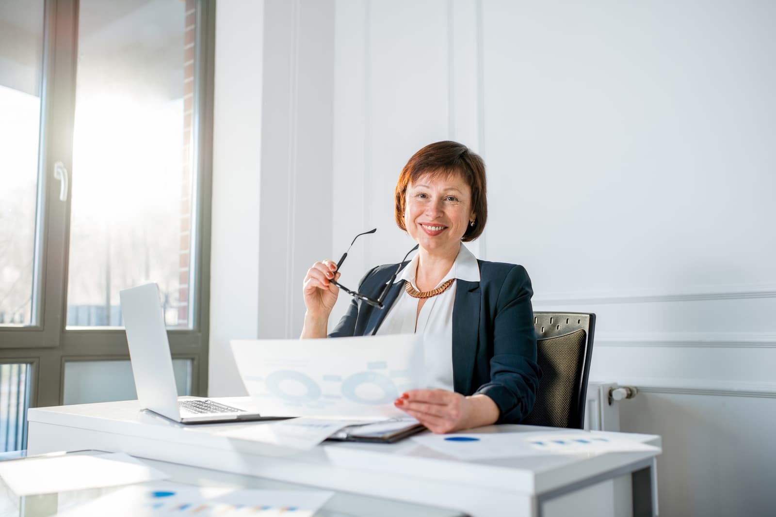A senior businesswoman comparing documents at her laptop