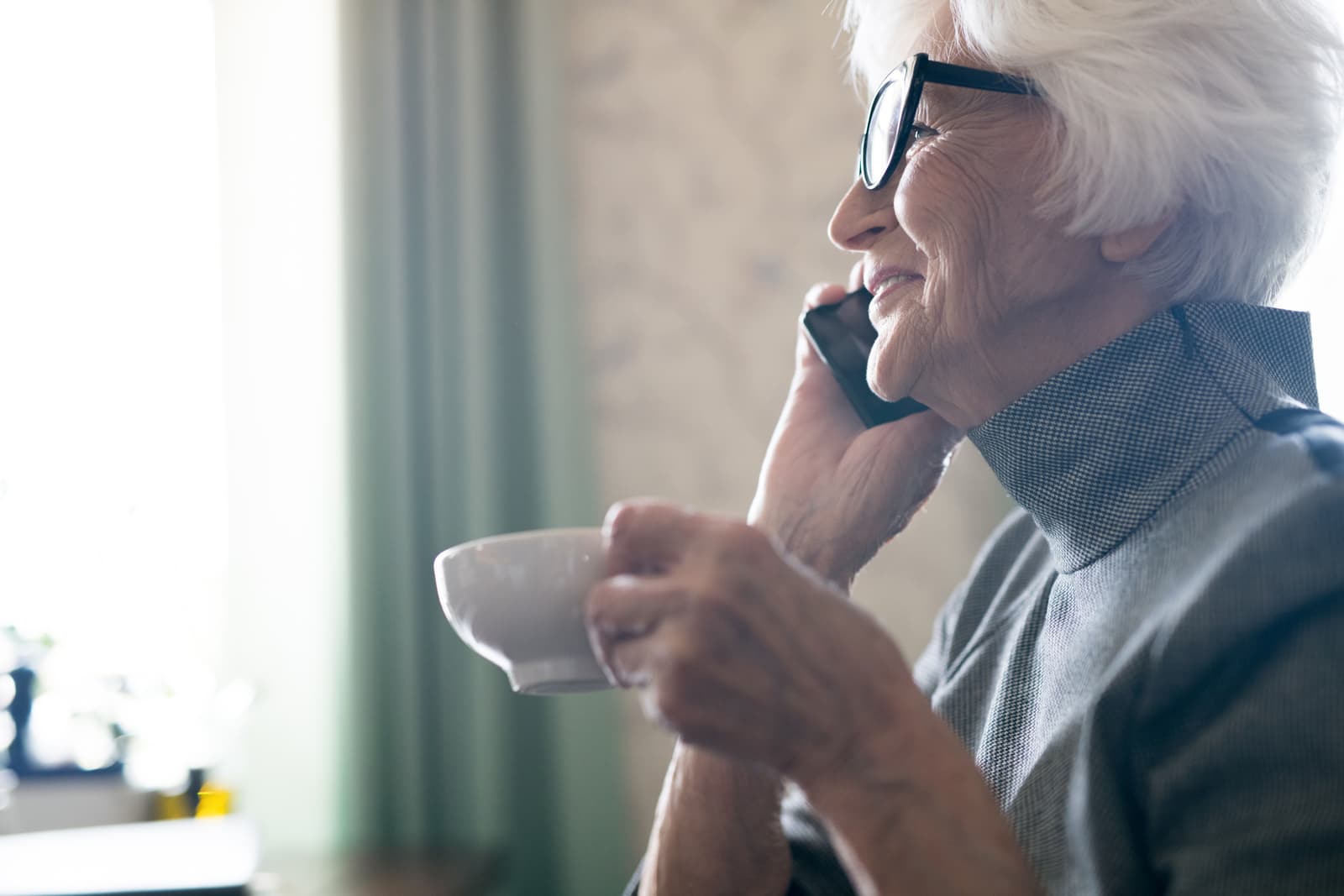 Side view of happy senior woman having a conversation on mobile phone while enjoying a cup of coffee
