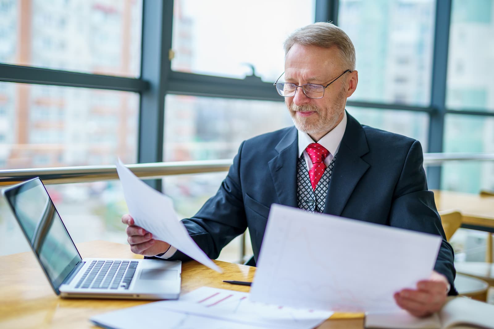 A mature businessman calmly reading his laptop by the office window