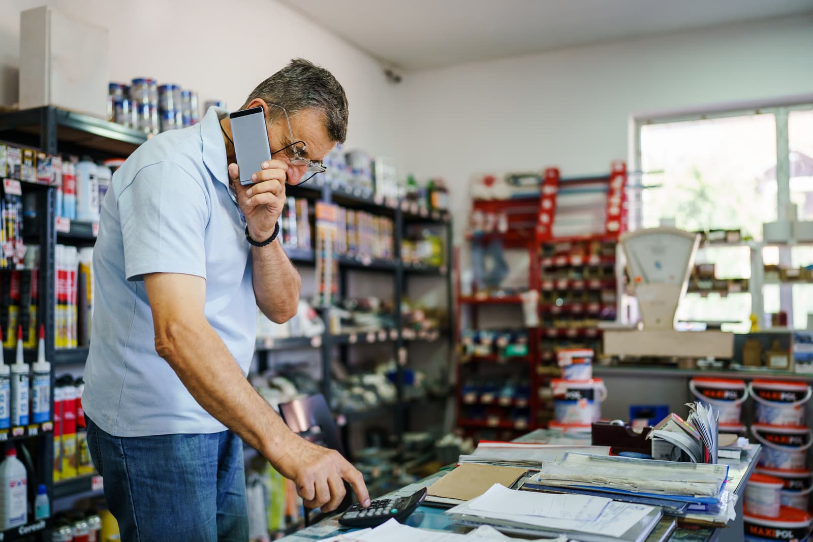 Side view of adult caucasian man senior salesman small business entrepreneur at his store standing by the desk using