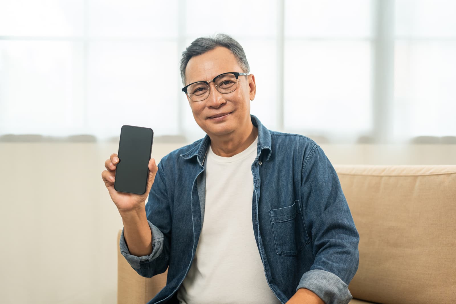 Handsome asian mature old man using smartphone on sofa in living room at home